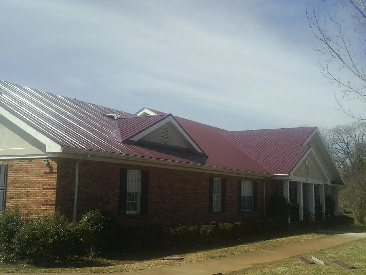 Red metal roof with gabled entries on a long brick building, from a Hail Damage Roof Repair job in Amboy