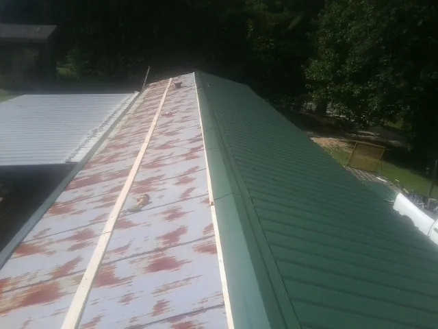 Old rusted panels beside newly installed green metal roofing — Wind Damage Roof Repair by Roofing Brothers in Amboy